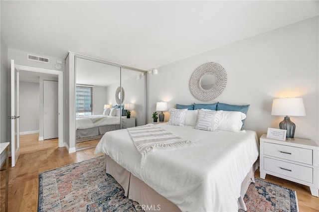 bedroom with light wood-style flooring, baseboards, visible vents, and a closet