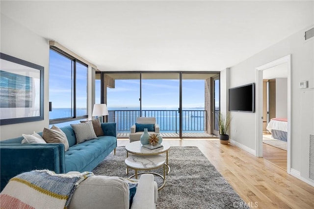 living room featuring visible vents, a water view, expansive windows, light wood finished floors, and baseboards