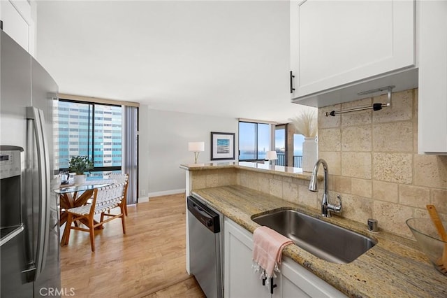 kitchen featuring backsplash, light stone countertops, stainless steel appliances, white cabinetry, and a sink