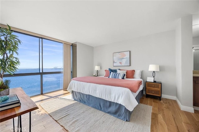 bedroom featuring light wood finished floors, floor to ceiling windows, baseboards, and a water view