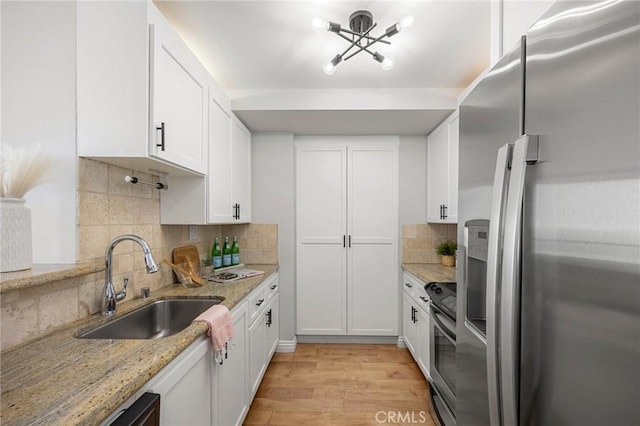 kitchen with light stone countertops, light wood-style flooring, a sink, appliances with stainless steel finishes, and white cabinetry