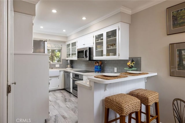 kitchen featuring glass insert cabinets, a breakfast bar, light countertops, appliances with stainless steel finishes, and a peninsula