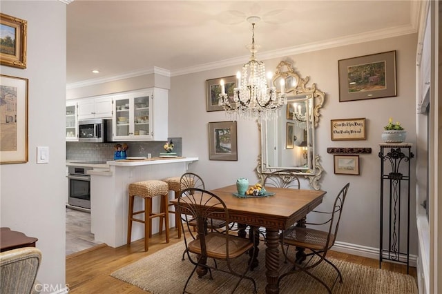 dining area with a notable chandelier, light wood-style floors, baseboards, and ornamental molding