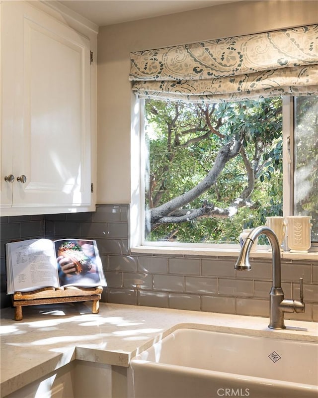 kitchen featuring tasteful backsplash, light stone countertops, white cabinetry, and a sink