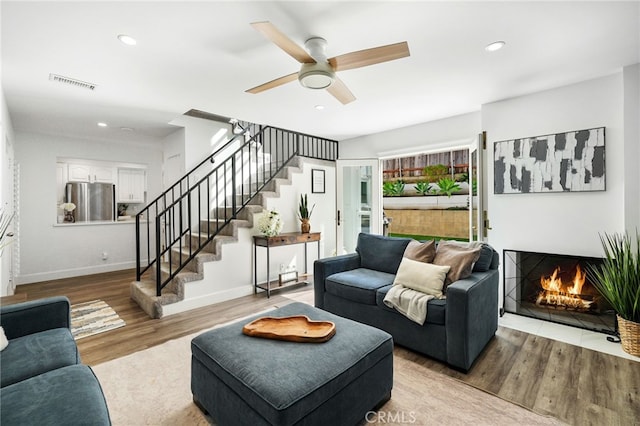 living area featuring stairway, wood finished floors, visible vents, recessed lighting, and a warm lit fireplace