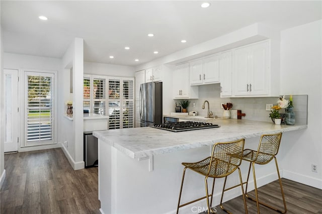 kitchen with dark wood finished floors, a peninsula, stainless steel appliances, decorative backsplash, and white cabinets