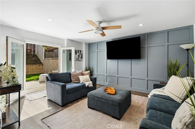 living area featuring a ceiling fan, a decorative wall, recessed lighting, and wood finished floors