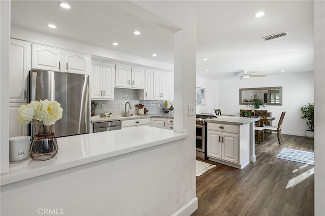 kitchen featuring visible vents, a peninsula, a sink, appliances with stainless steel finishes, and white cabinetry