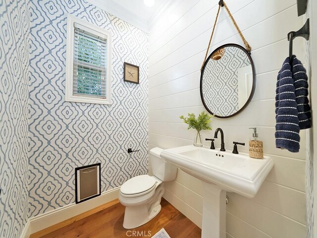 half bathroom featuring baseboards, toilet, wood finished floors, and ornamental molding