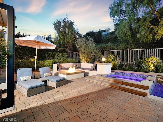 view of patio with an in ground hot tub, a fire pit, and fence