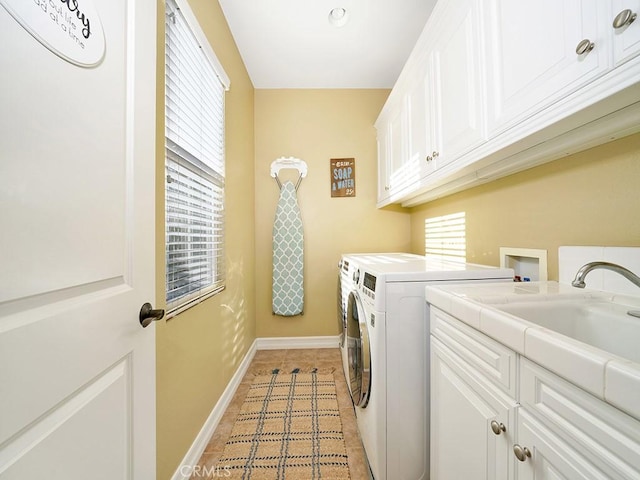 clothes washing area featuring a sink, washing machine and dryer, cabinet space, light tile patterned flooring, and baseboards