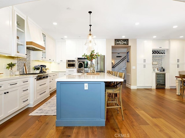 kitchen featuring dark wood-type flooring, wine cooler, a breakfast bar, white cabinets, and stainless steel appliances