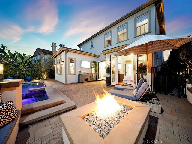 back of property at dusk with a fenced in pool, an outdoor kitchen, stucco siding, a fire pit, and a patio area