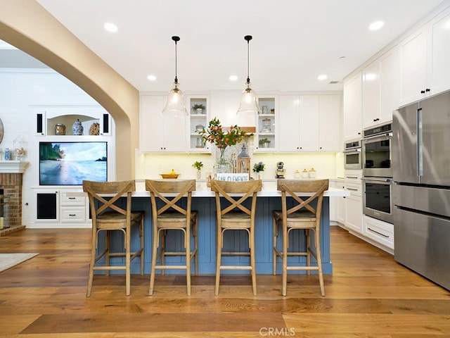 kitchen featuring wood finished floors, a center island, appliances with stainless steel finishes, white cabinets, and glass insert cabinets