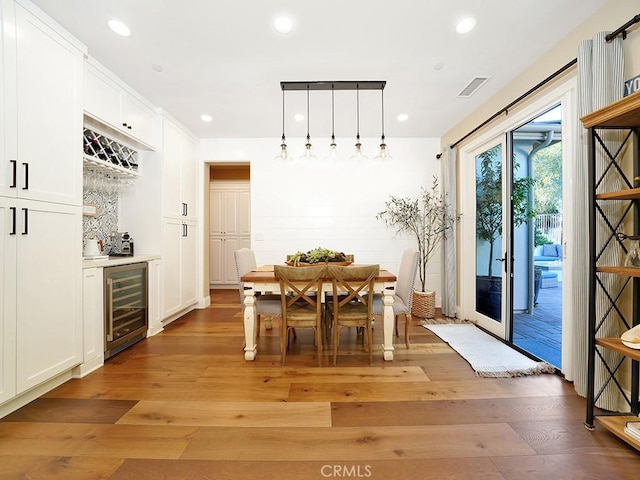 dining room featuring beverage cooler, visible vents, light wood finished floors, recessed lighting, and a bar