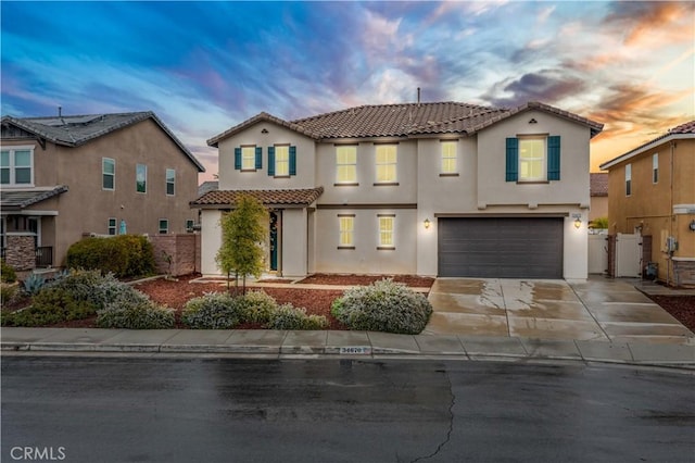 mediterranean / spanish-style home with an attached garage, fence, a tile roof, stucco siding, and driveway