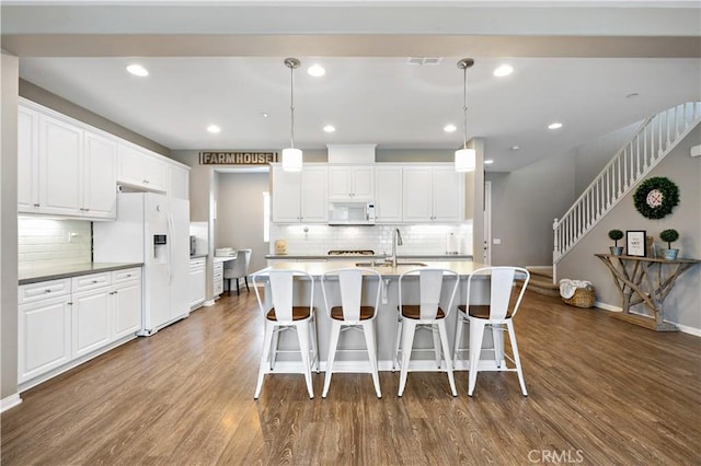 kitchen featuring a breakfast bar, a sink, wood finished floors, white appliances, and white cabinets