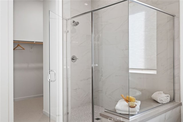 full bath featuring a marble finish shower, a walk in closet, and baseboards