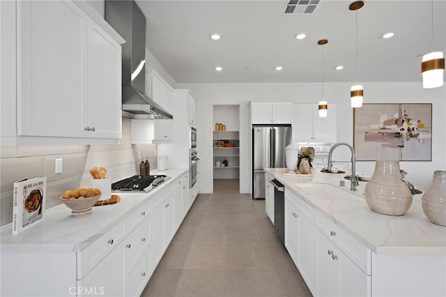 kitchen featuring visible vents, a sink, appliances with stainless steel finishes, wall chimney exhaust hood, and tasteful backsplash