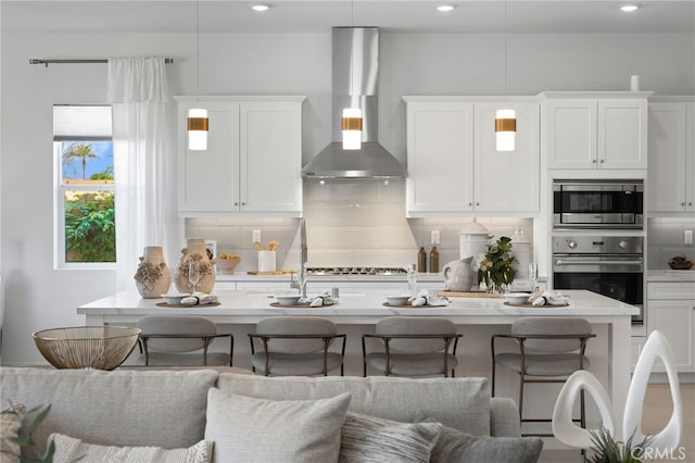 kitchen featuring tasteful backsplash, a breakfast bar, white cabinets, and wall chimney range hood