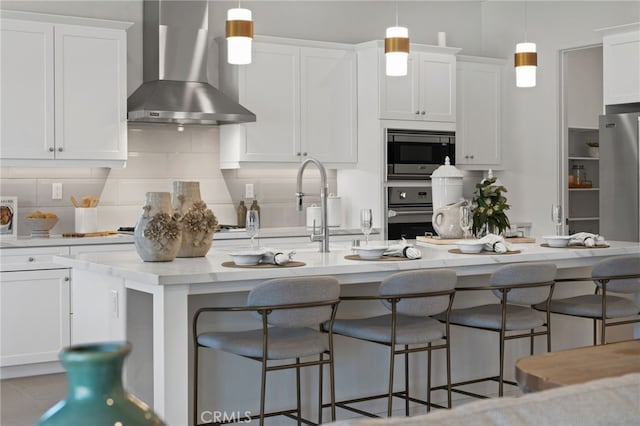 kitchen with tasteful backsplash, stainless steel microwave, wall oven, white cabinets, and wall chimney exhaust hood