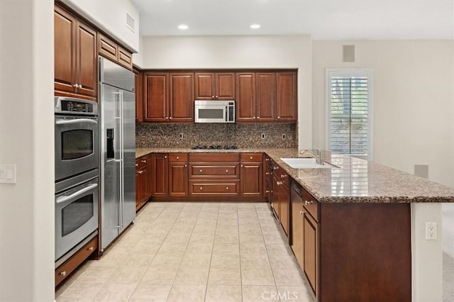 kitchen with a sink, backsplash, stainless steel appliances, a peninsula, and stone counters