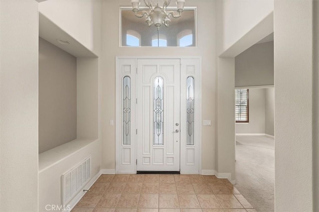 carpeted foyer featuring visible vents, baseboards, a high ceiling, and a chandelier