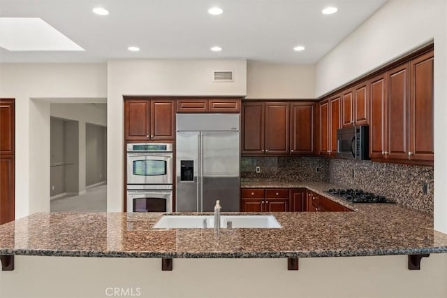 kitchen featuring a kitchen bar, dark stone countertops, backsplash, and appliances with stainless steel finishes