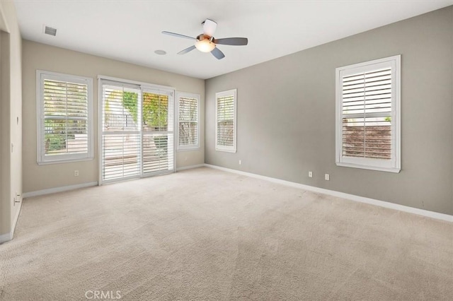 carpeted empty room featuring visible vents, baseboards, a healthy amount of sunlight, and a ceiling fan