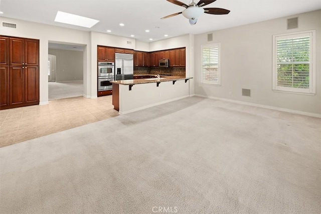 kitchen with a breakfast bar area, a ceiling fan, visible vents, appliances with stainless steel finishes, and light colored carpet