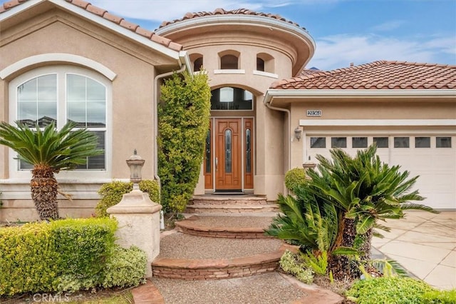 doorway to property with stucco siding, a garage, concrete driveway, and a tile roof