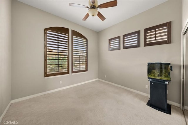 carpeted empty room featuring baseboards and a ceiling fan