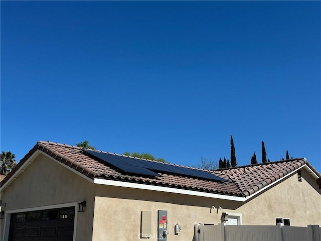 view of property exterior with solar panels, a tile roof, fence, and stucco siding