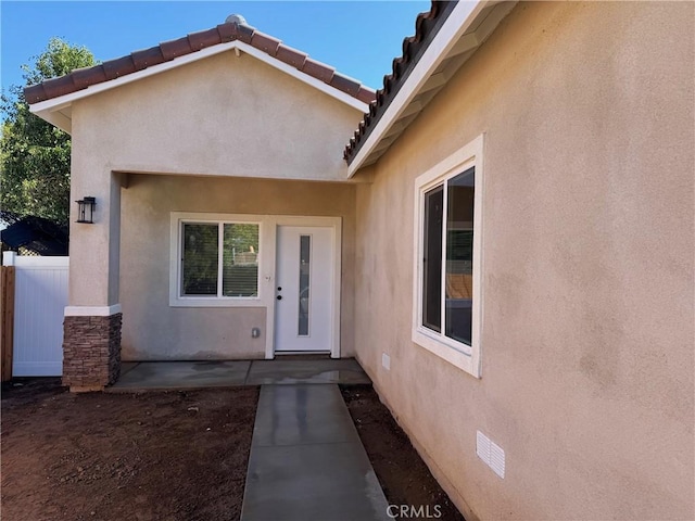 entrance to property featuring fence, crawl space, a tiled roof, stucco siding, and a patio area