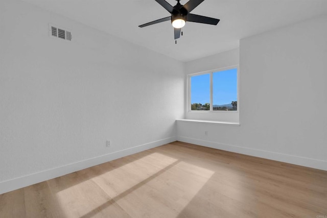 spare room featuring light wood finished floors, visible vents, a ceiling fan, and baseboards