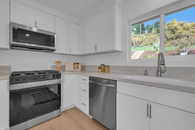 kitchen featuring a sink, stainless steel appliances, light countertops, white cabinets, and light wood-type flooring