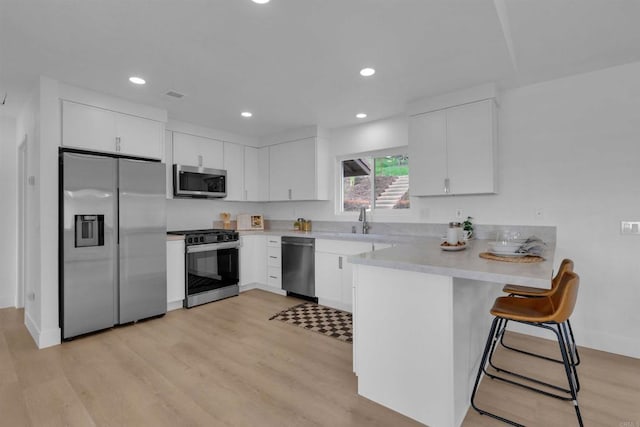 kitchen featuring light wood-type flooring, stainless steel appliances, a peninsula, white cabinets, and light countertops