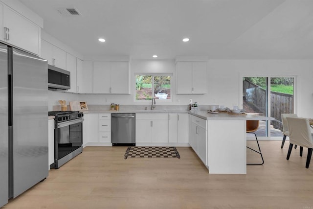 kitchen featuring visible vents, a kitchen bar, appliances with stainless steel finishes, a peninsula, and a sink