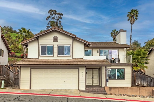 view of front of home with a balcony, an attached garage, a chimney, and fence