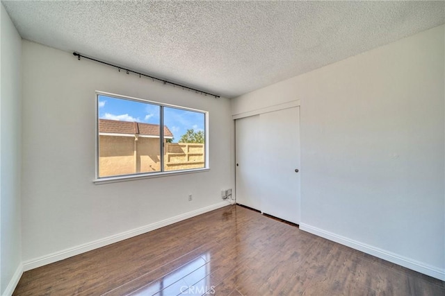 unfurnished bedroom with a textured ceiling, wood finished floors, a closet, and baseboards