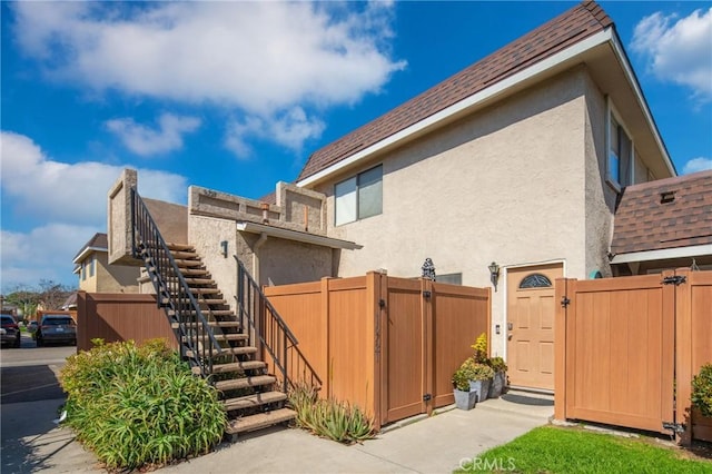 view of side of home with stairway, stucco siding, and a gate