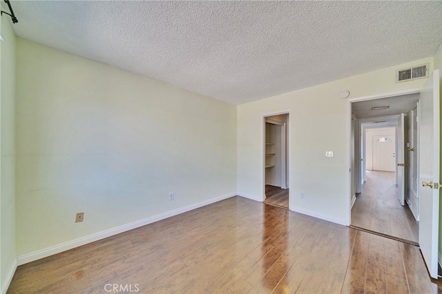 empty room with visible vents, a textured ceiling, baseboards, and wood-type flooring