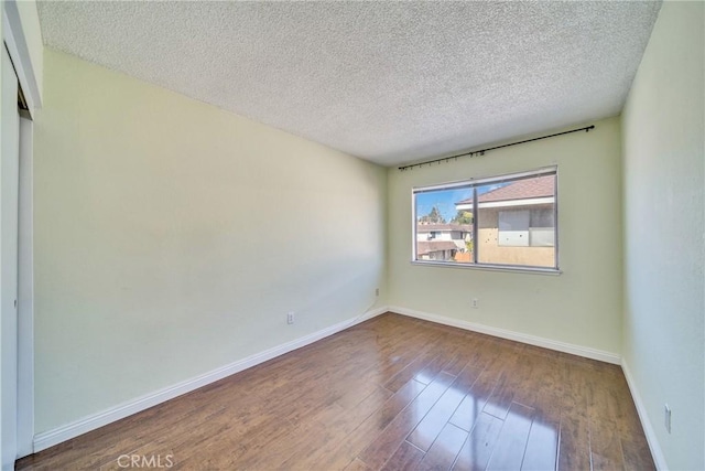 unfurnished room with a textured ceiling, baseboards, and wood finished floors