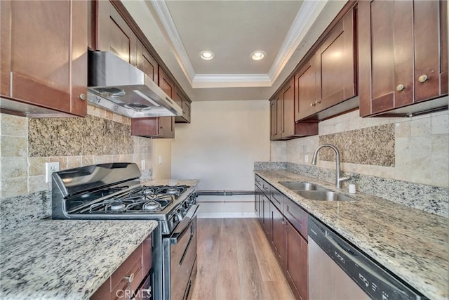 kitchen with a sink, ornamental molding, stainless steel appliances, a raised ceiling, and wall chimney exhaust hood