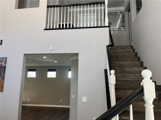 staircase featuring visible vents, wood finished floors, a high ceiling, crown molding, and baseboards