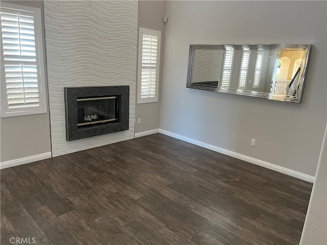 unfurnished living room with a glass covered fireplace, baseboards, and wood finished floors