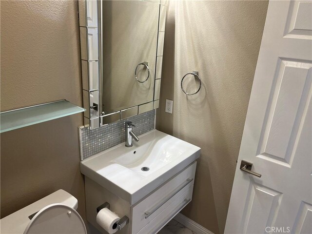 bathroom with vanity, toilet, a textured wall, and backsplash