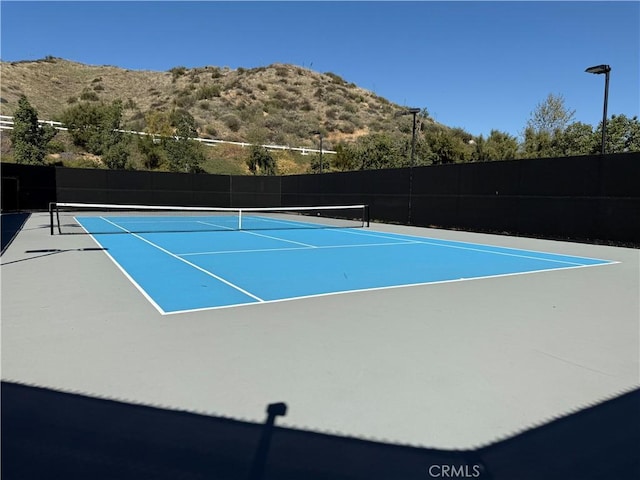 view of tennis court with a mountain view and fence