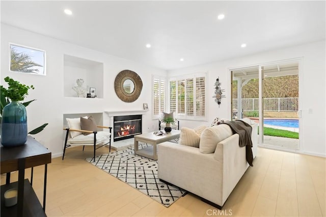 living area featuring recessed lighting, baseboards, light wood-style floors, and a glass covered fireplace