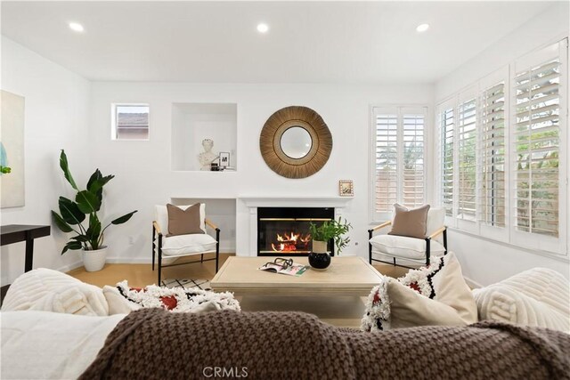 living area with a glass covered fireplace, wood finished floors, recessed lighting, and baseboards